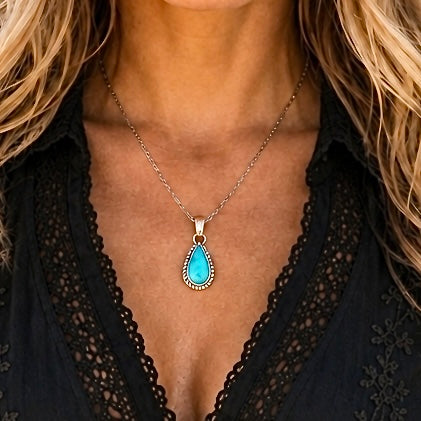 Necklace with a blue teardrop pendant worn by a person in a black lace top.